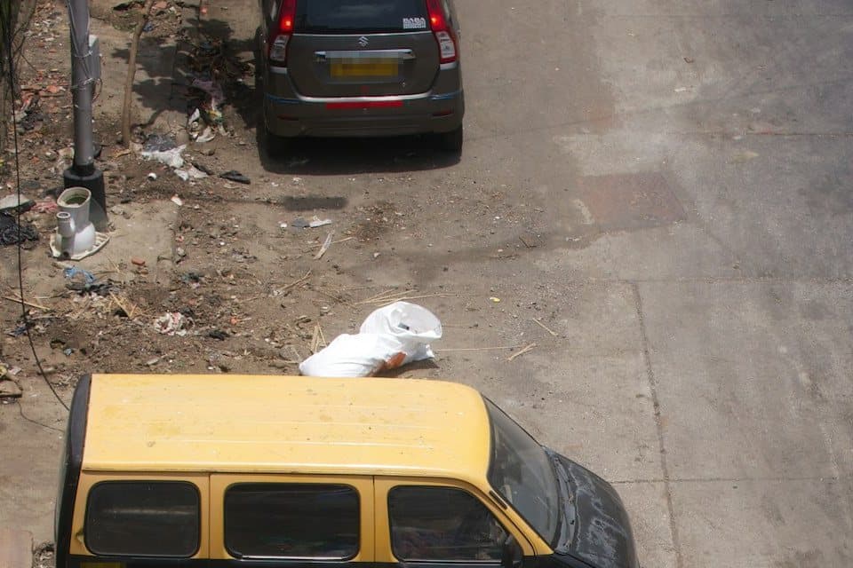 A single white bag of garbage dumped at the edge of a city street, seen from above