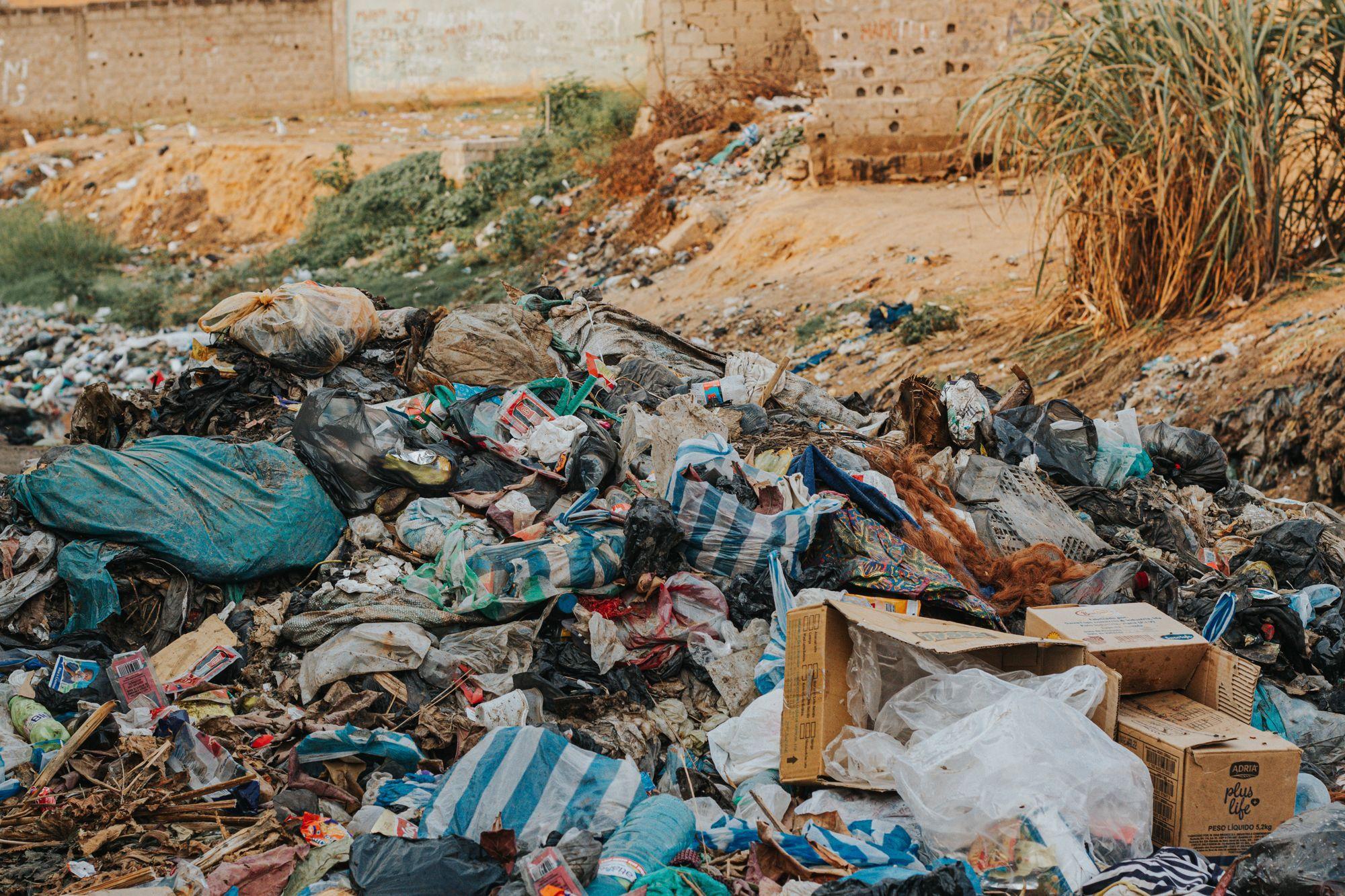 Mixed waste dumped on open ground: plastic sacks, cardboard boxes, food scraps, cloth and broken rubble together