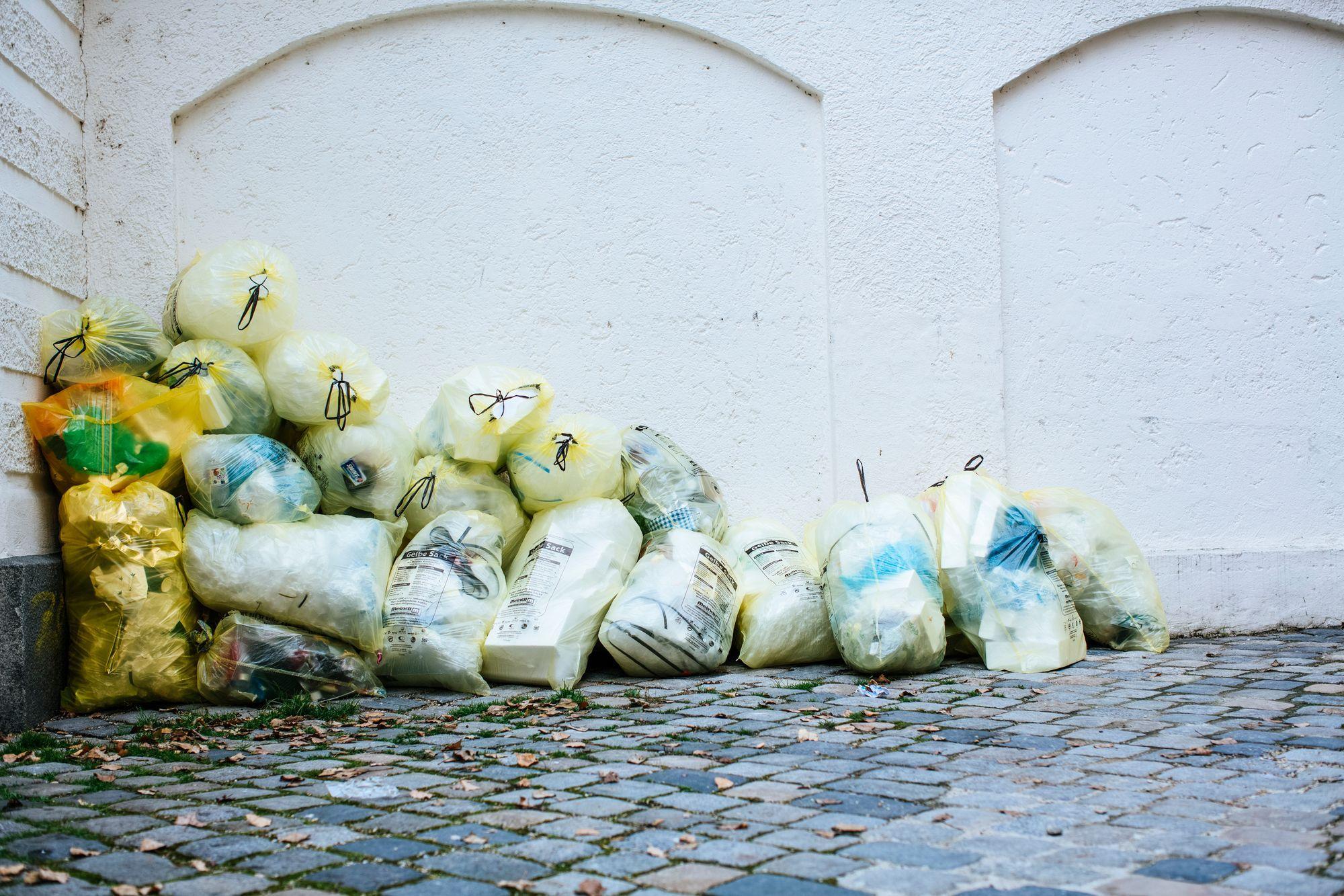Bags of garbage dumped along the foot of a wall on a street