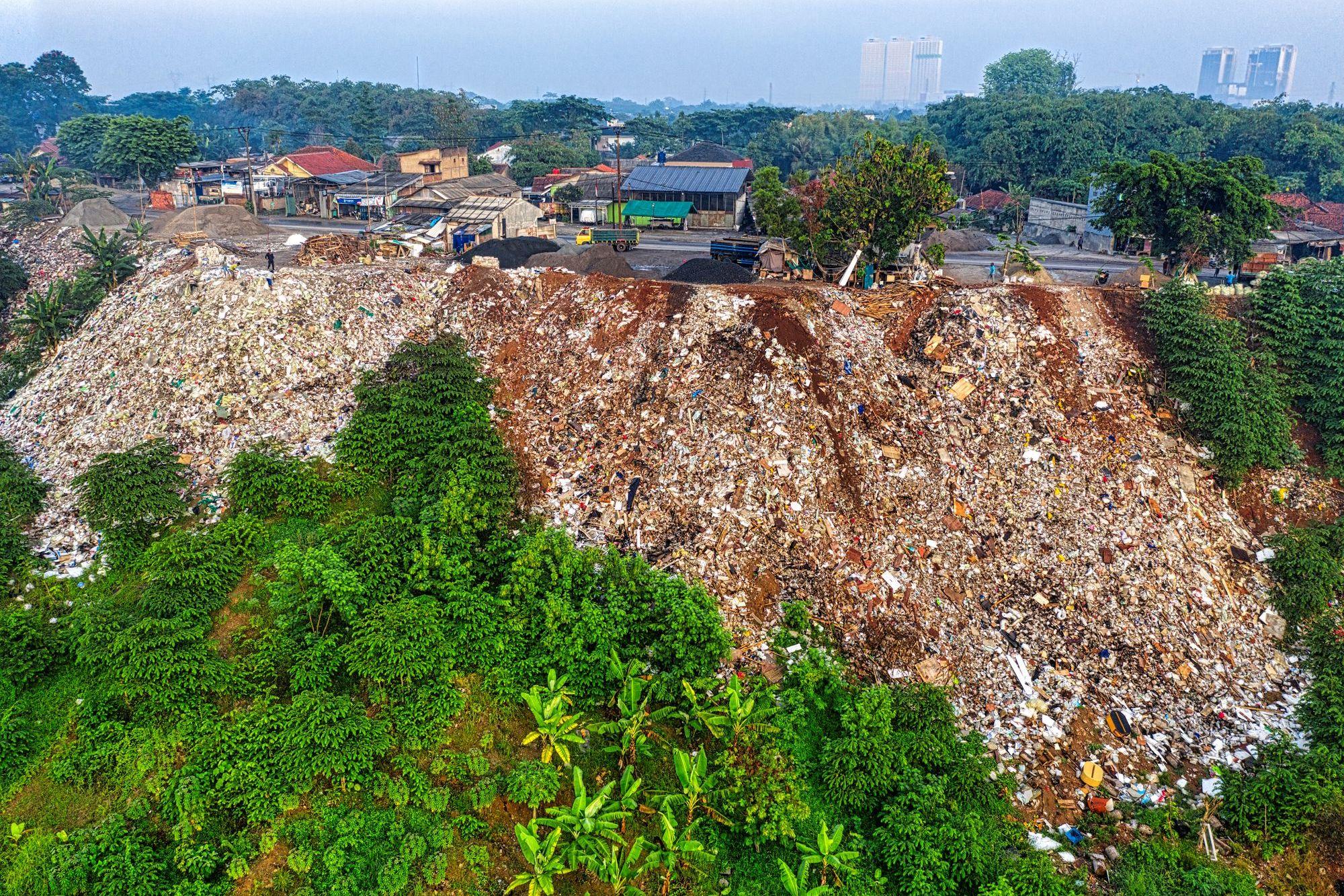 A garbage dump the size of a hill on the edge of a town, houses and towers behind it