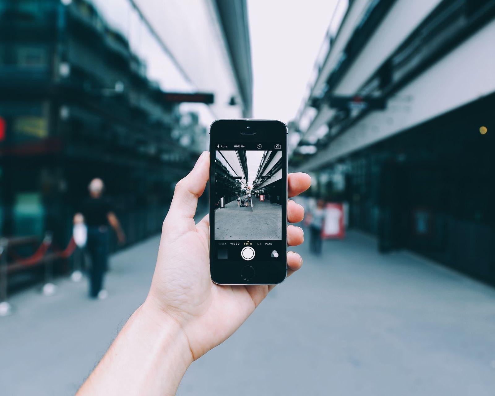 A hand holding up a phone, taking a photo of a city street