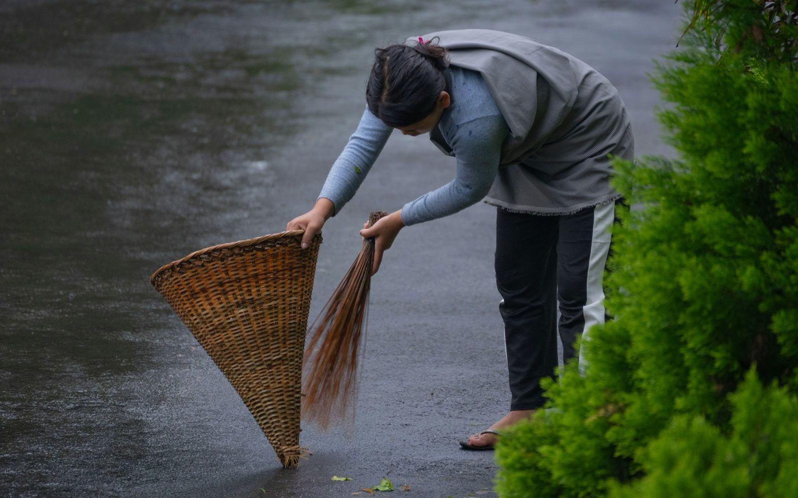 A woman sweeping a wet lane with a broom and a cane basket